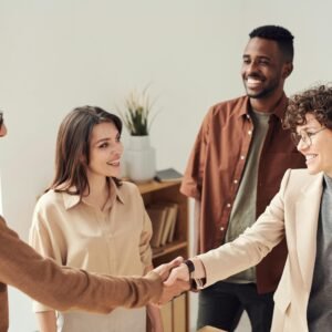 Four colleagues smiling and shaking hands in a bright office setting.